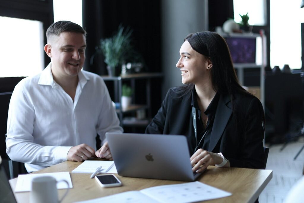 A man and a woman sitting at a table with a laptop planning optimistically unaware of the planning fallacy