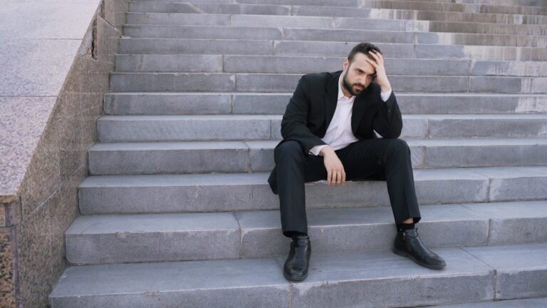 Career Misalignment: Why Your Shiny Job Feels Dead Inside 6 Man in suit sitting on outdoor stairs looking down.