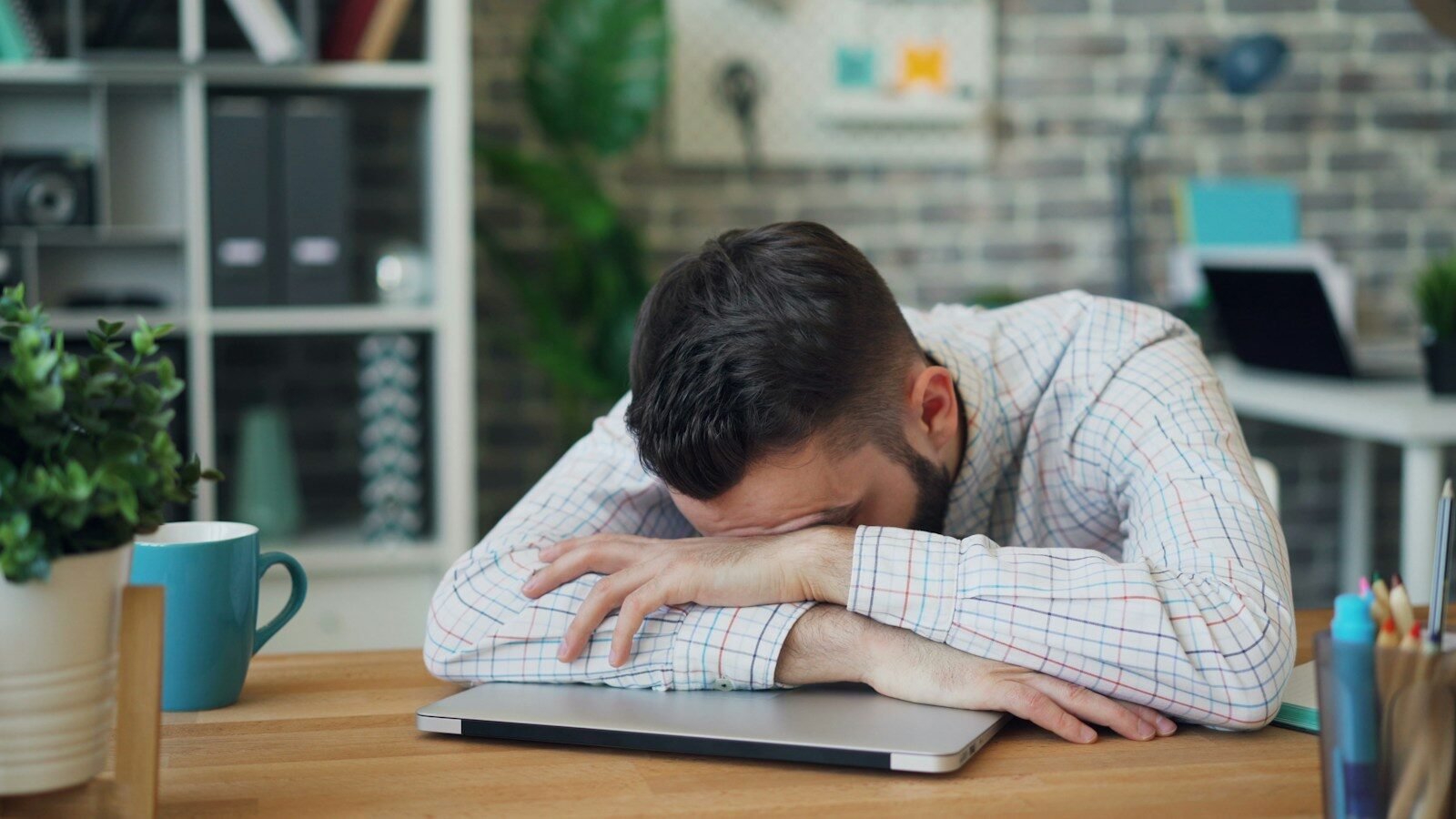 An exhausted professional resting his head on a closed laptop, a picture of everything being priority one